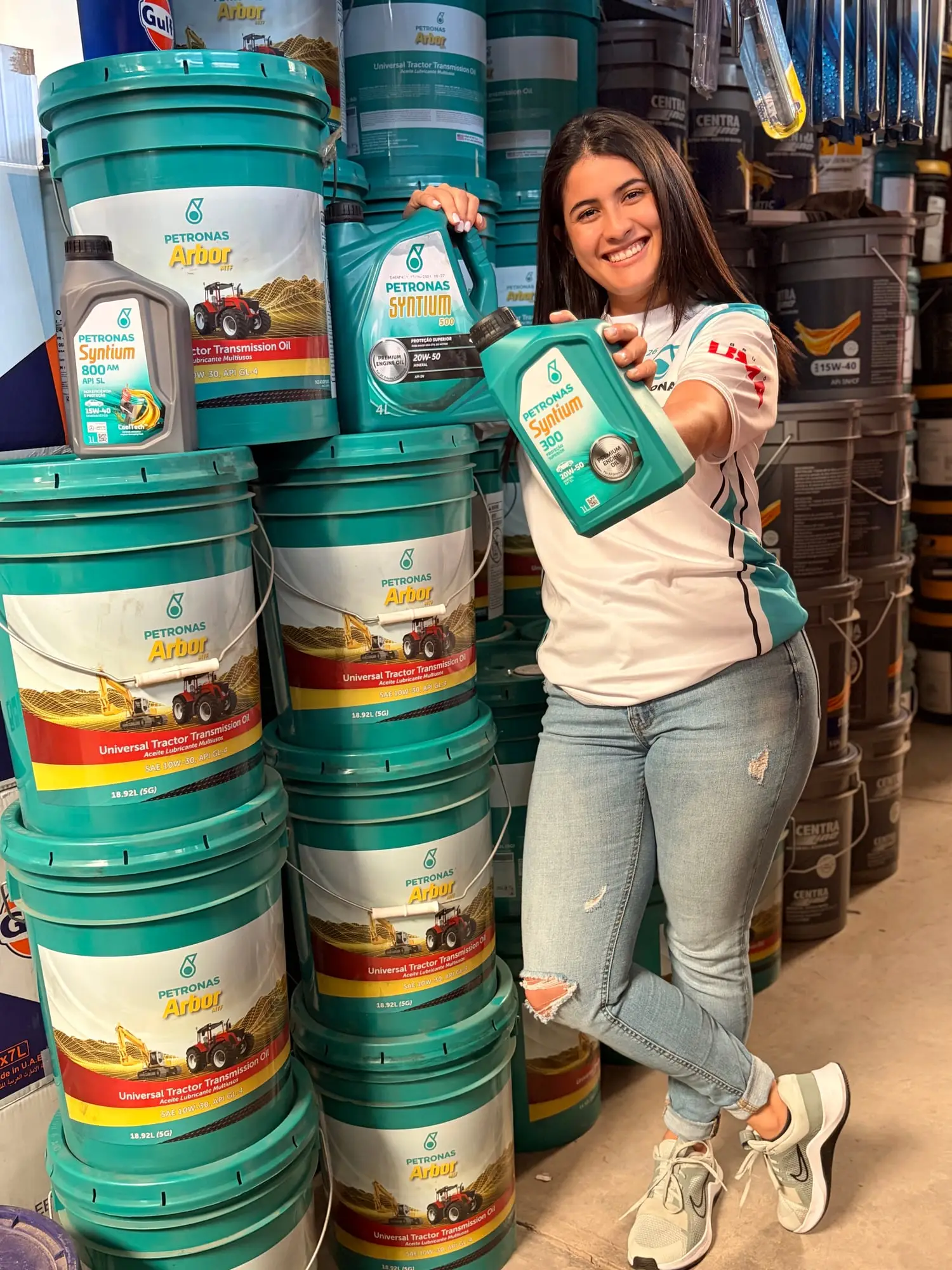 Asesora de CR Autos con envases de aceite Petronas Syntium frente a cubetas de lubricante Petronas